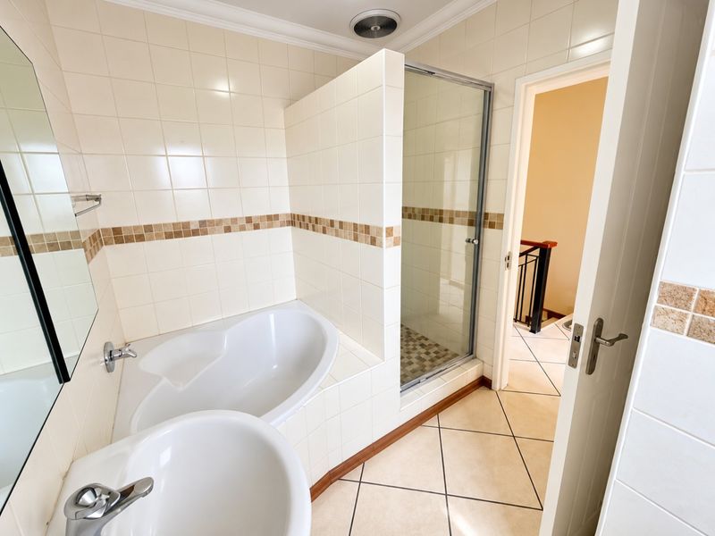 A clean, functional bathroom featuring a built-in bathtub, separate shower enclosure, and tiled finishes throughout.