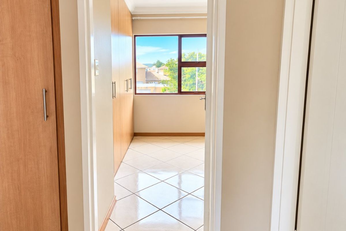 A bright, empty bedroom featuring tiled flooring, built-in wooden cupboards, and a window providing natural light and neighborhood views.
