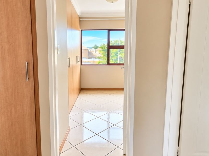 A bright, empty bedroom featuring tiled flooring, built-in wooden cupboards, and a window providing natural light and neighborhood views.