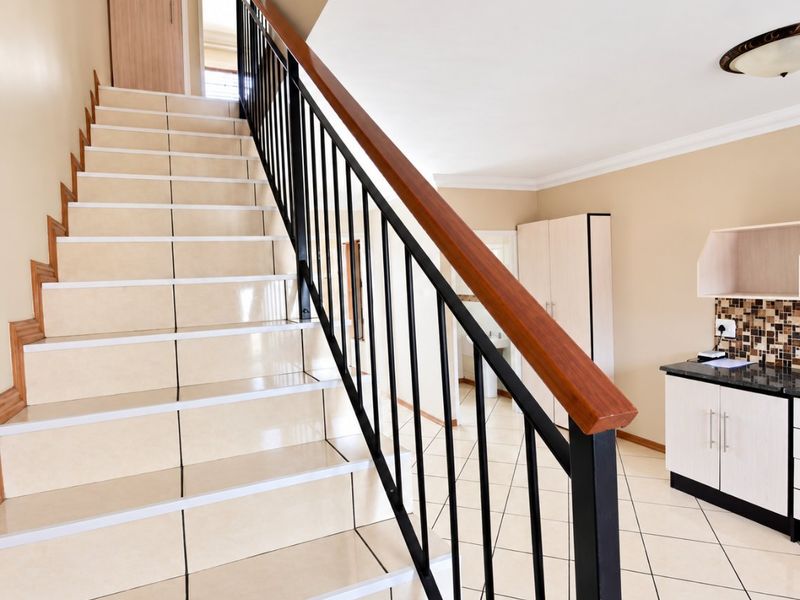 A bright hallway featuring a tiled staircase with a modern metal and wood balustrade, leading to an open area with built-in cabinetry.