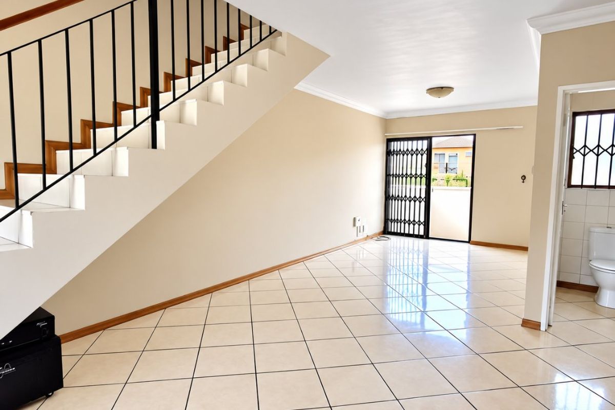 Spacious open-plan living area featuring ceramic tiled flooring, a staircase with a metal balustrade, and direct access to an outdoor area via a security gate.