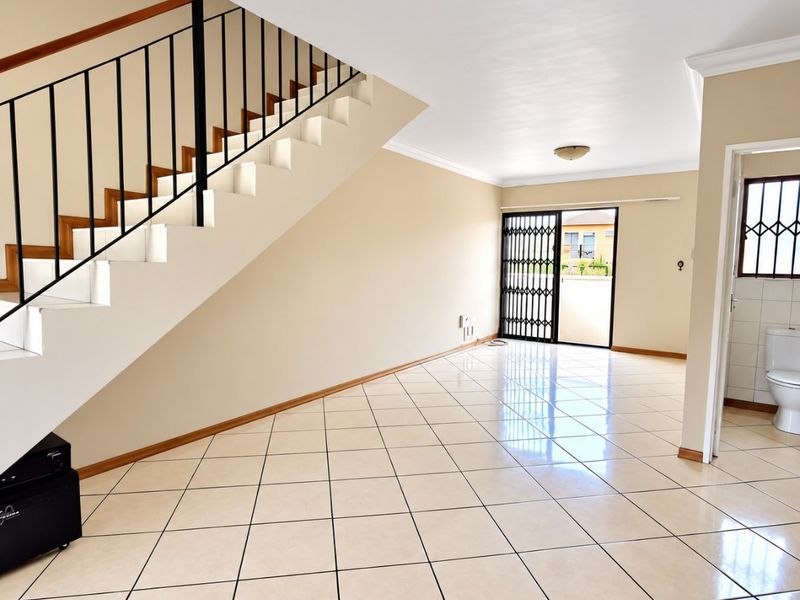 Spacious open-plan living area featuring ceramic tiled flooring, a staircase with a metal balustrade, and direct access to an outdoor area via a security gate.