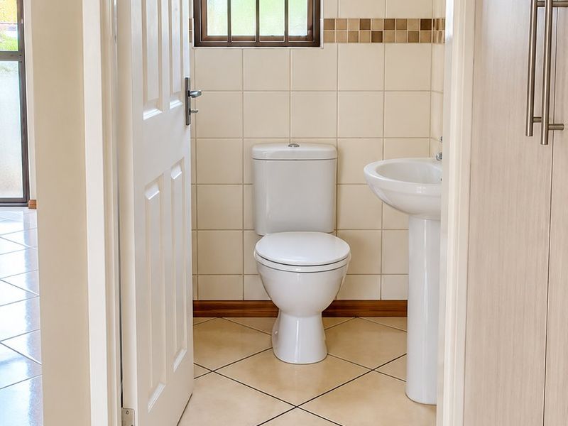 A clean and functional guest bathroom featuring a pedestal basin, toilet, and neutral ceramic tiling throughout.