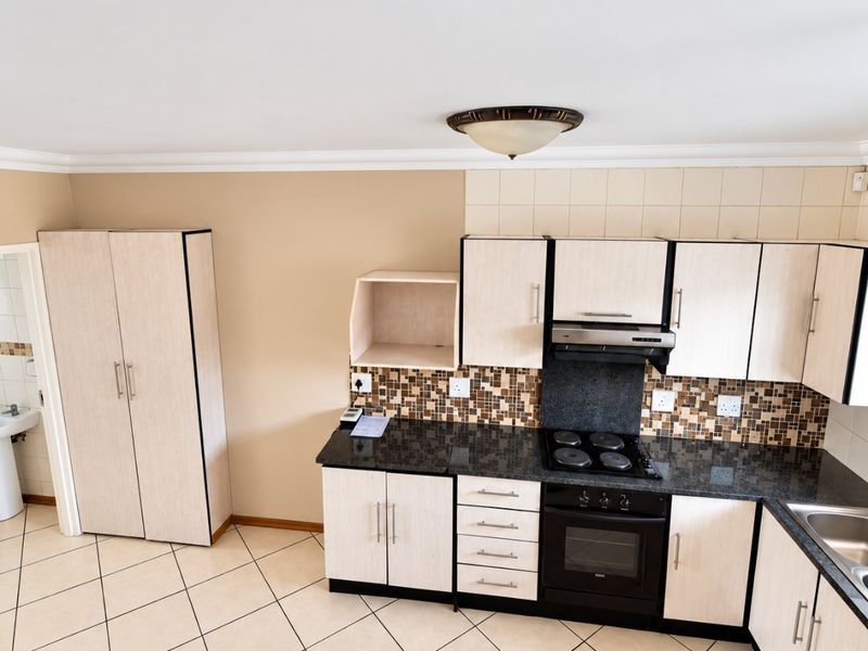 A functional kitchen featuring light wood-finish cabinetry, granite countertops, a mosaic tile backsplash, and built-in cooking appliances with ceramic tiled flooring.