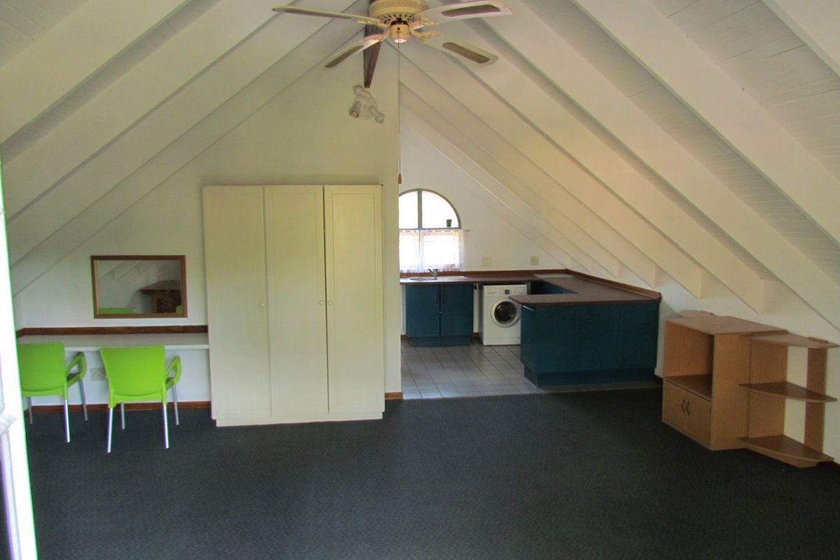 Open plan living area featuring a vaulted ceiling, ceiling fan, built-in desk, wardrobe, and a functional kitchen area with tiled flooring.