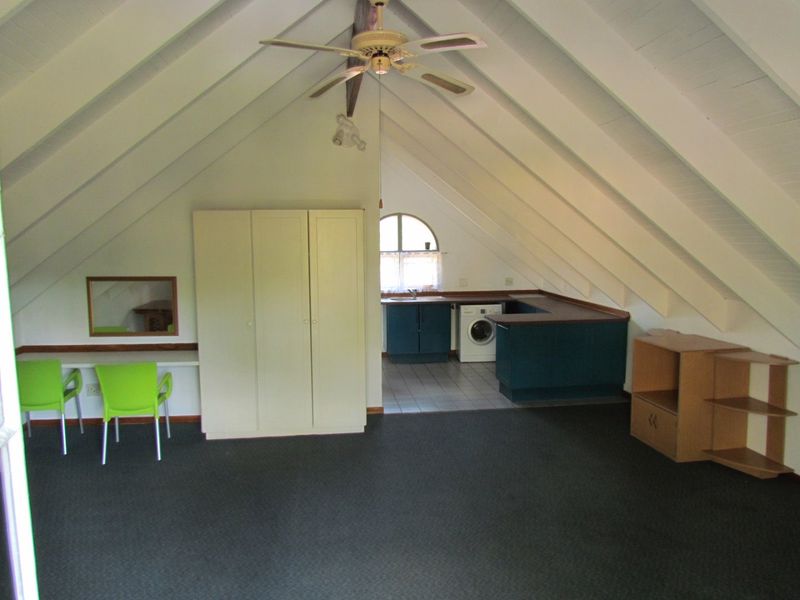 Open plan living area featuring a vaulted ceiling, ceiling fan, built-in desk, wardrobe, and a functional kitchen area with tiled flooring.