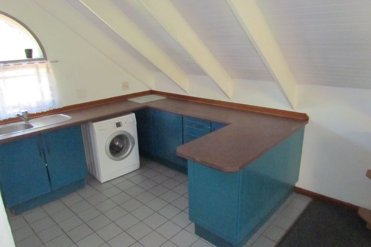 A compact kitchen area featuring blue built-in cabinetry, a laminate countertop, and a stainless steel sink, set under a sloped ceiling with exposed rafters.