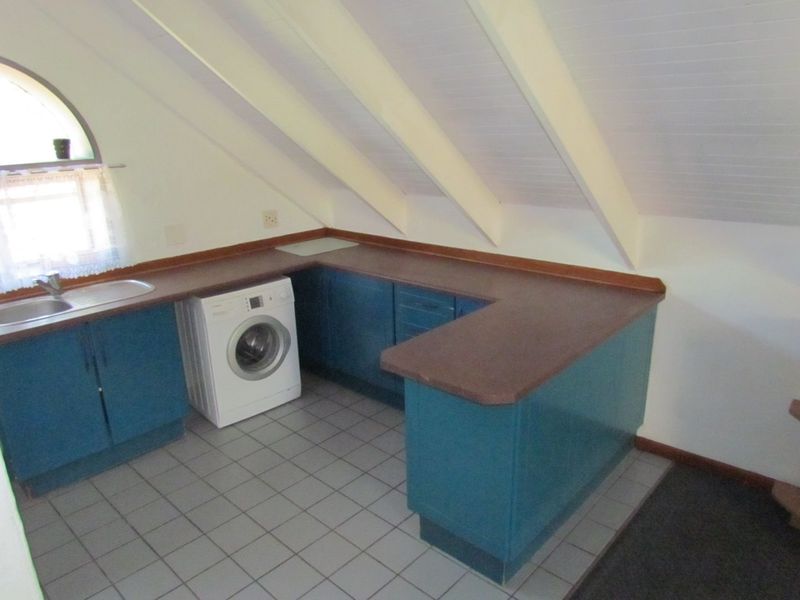 A compact kitchen area featuring blue built-in cabinetry, a laminate countertop, and a stainless steel sink, set under a sloped ceiling with exposed rafters.