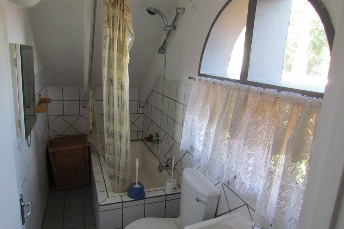 Compact bathroom featuring a built-in bathtub with shower attachment, pedestal sink, toilet, and an arched window with tiled finishes.