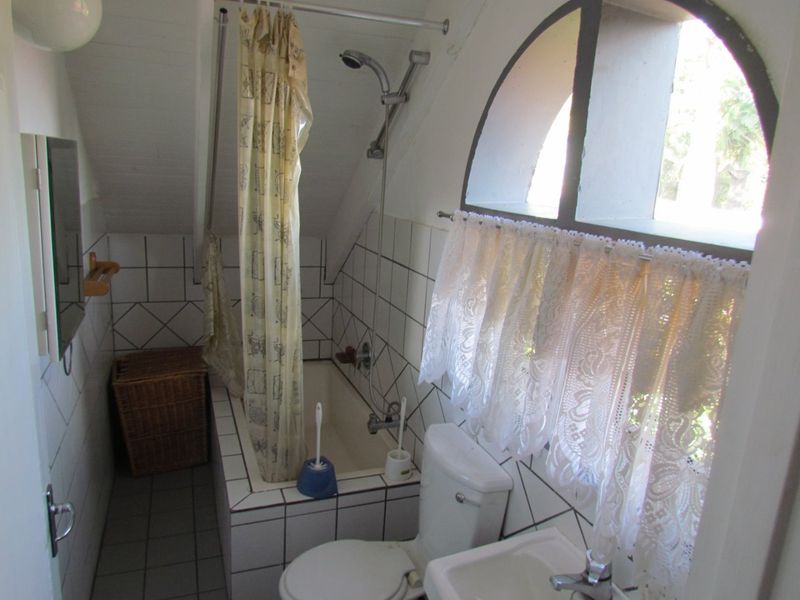 Compact bathroom featuring a built-in bathtub with shower attachment, pedestal sink, toilet, and an arched window with tiled finishes.