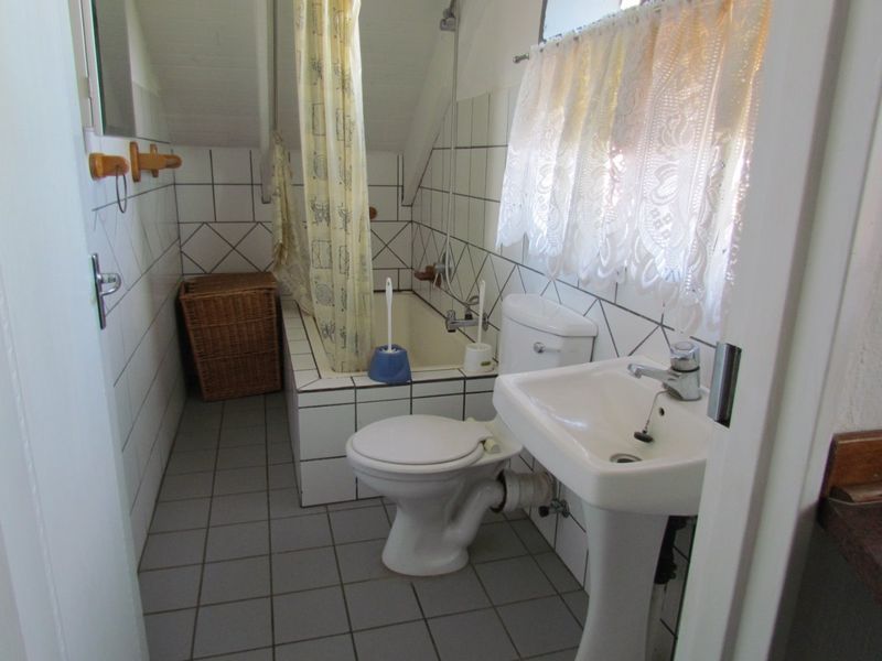 A compact bathroom featuring a pedestal basin, toilet, and a tiled bathtub with shower mixer, finished with dated wall and floor tiling.