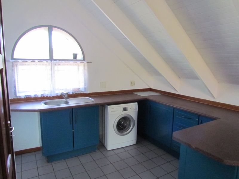 A functional kitchen area featuring blue cabinetry, laminate countertops, a stainless steel sink, and an arched window set under a pitched ceiling with exposed rafters.