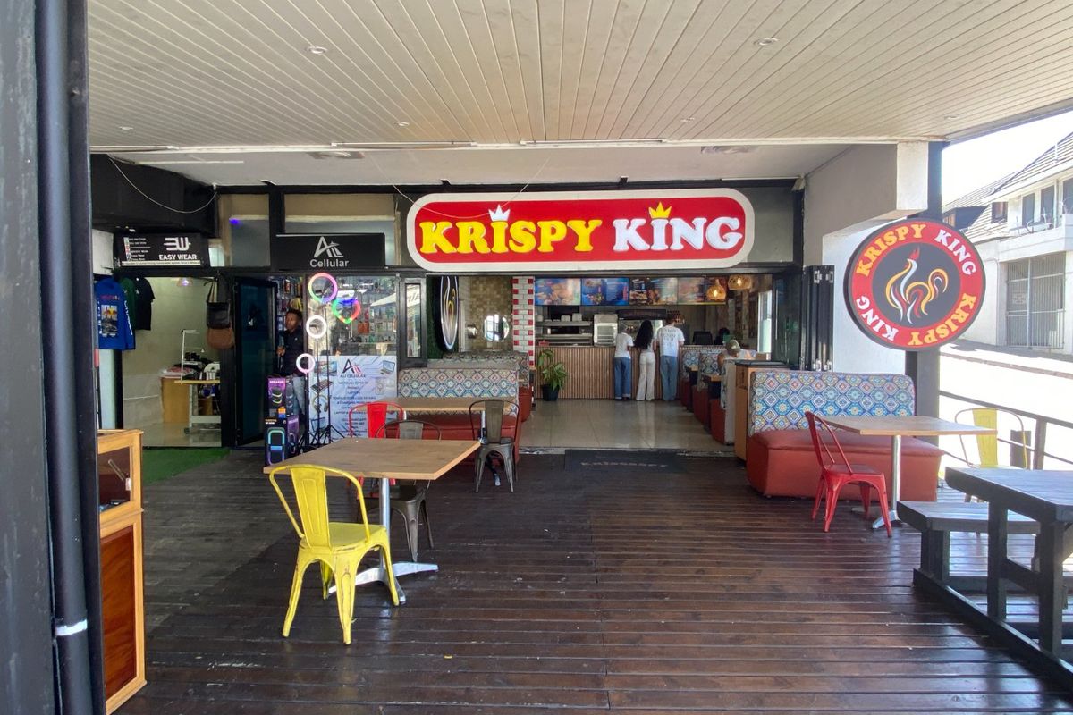 A commercial outdoor patio area featuring timber decking and covered ceiling, serving as an entrance to a retail and food service establishment.
