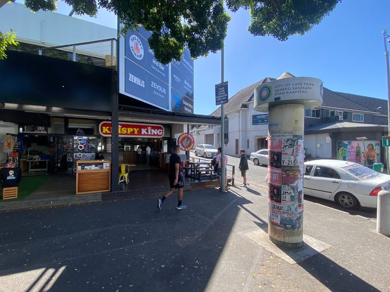 Street-level view of a commercial building facade featuring multiple storefronts and signage in a busy urban area.