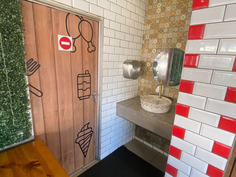 A commercial bathroom featuring a concrete vanity with a decorative vessel sink, brass faucet, and a mix of subway and patterned accent tiling.