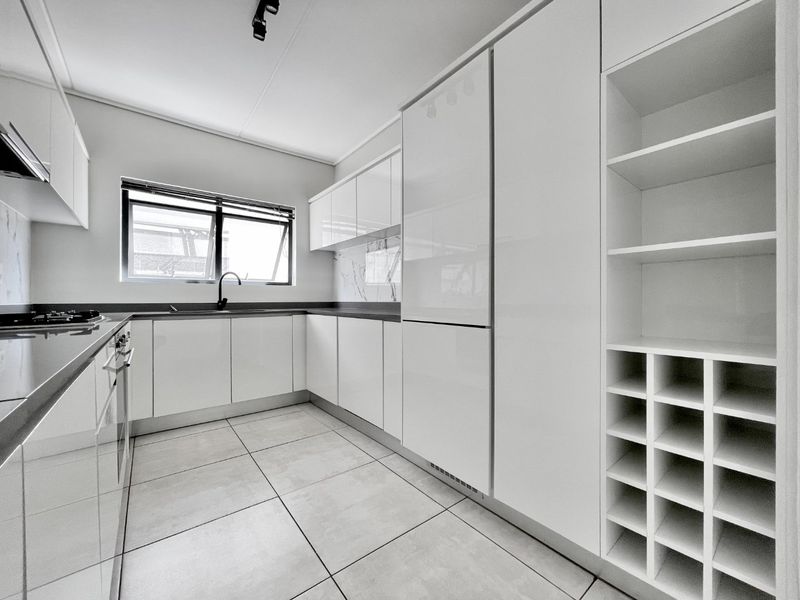 Modern kitchen featuring sleek white cabinetry, integrated wine storage, stone countertops, marble-look splashback, and high-quality built-in appliances.