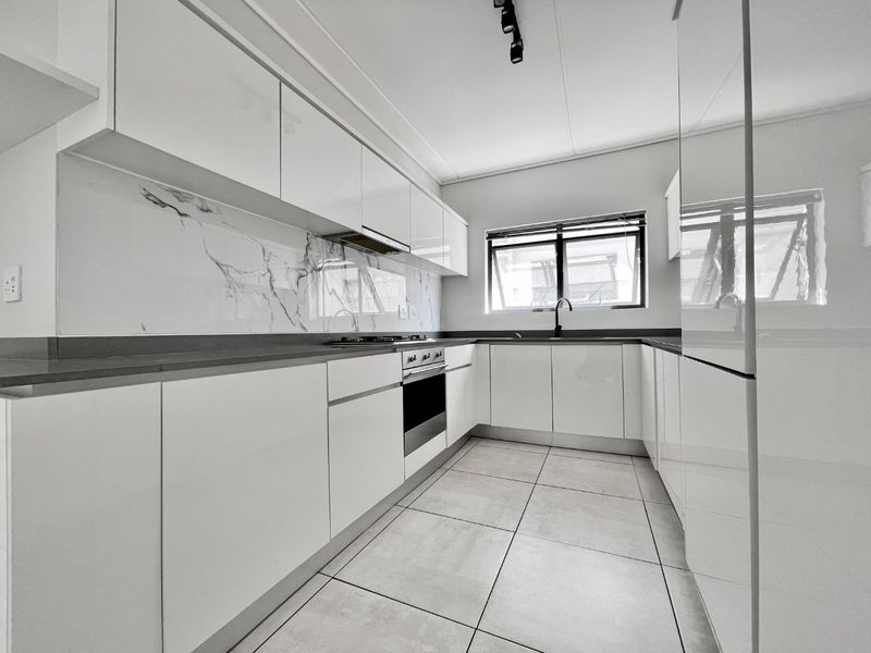 Modern kitchen featuring sleek white cabinetry, marble-look splashback, stone countertops, built-in oven, gas hob, and high-quality tiled flooring.