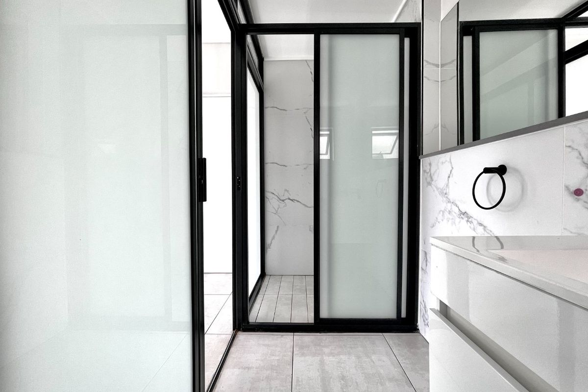 Modern bathroom featuring marble-look wall tiles, large format floor tiles, a sleek vanity with integrated basin, and a contemporary black-framed sliding glass door.