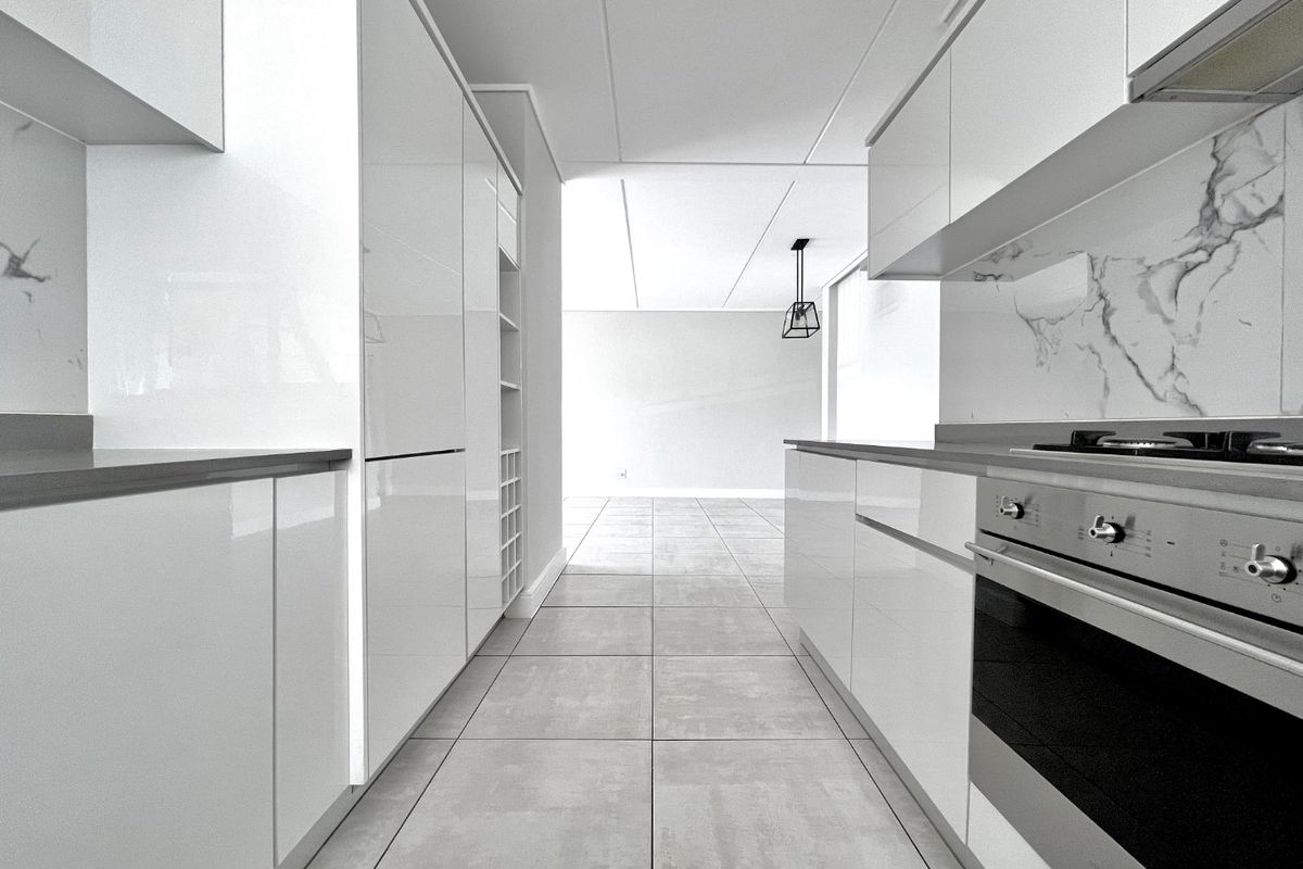 Modern galley-style kitchen featuring high-gloss white cabinetry, marble-look splashbacks, integrated gas cooktop, and sleek tiled flooring in an open-plan layout.