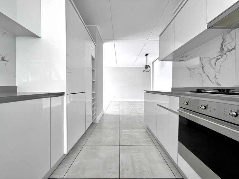 Modern galley-style kitchen featuring high-gloss white cabinetry, marble-look splashbacks, integrated gas cooktop, and sleek tiled flooring in an open-plan layout.