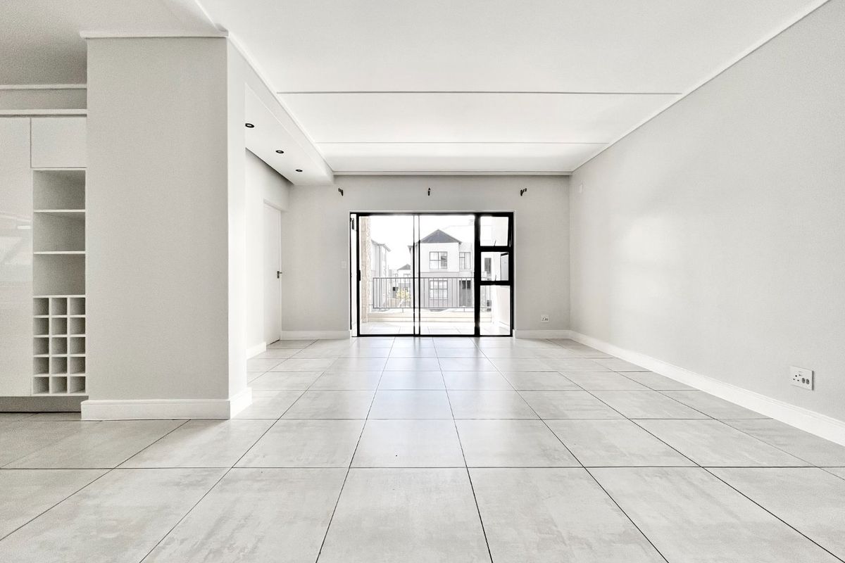 A bright, spacious, and empty living area featuring modern tiled floors, built-in shelving, and a sliding glass door leading to an outdoor space.