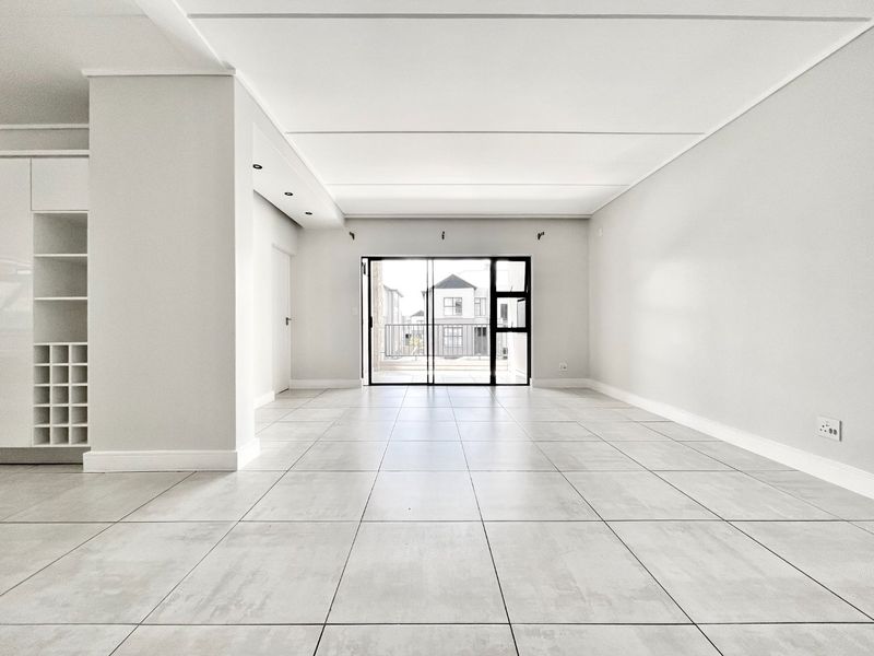 A bright, spacious, and empty living area featuring modern tiled floors, built-in shelving, and a sliding glass door leading to an outdoor space.