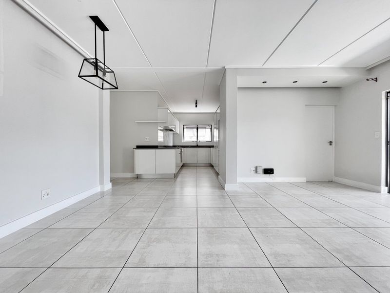 A bright and spacious open-plan living and kitchen area featuring modern tiled flooring, neutral finishes, and clean, contemporary lines throughout the space.