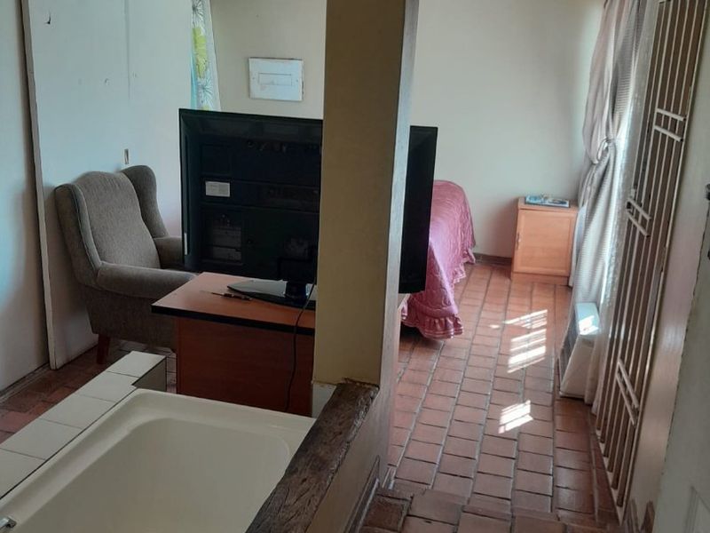 A bedroom featuring terracotta floor tiles, built-in cupboards, and an integrated bathtub, presenting a dated layout that could benefit from modern renovation.