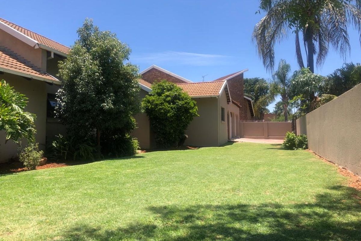 A spacious rear garden featuring a well-maintained lawn, mature trees, and a secure boundary wall, providing a private outdoor area.