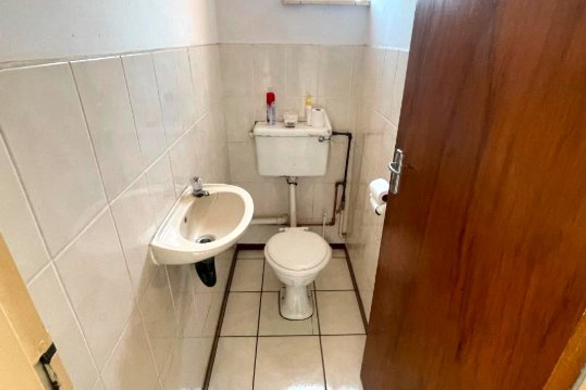 A compact, functional guest bathroom featuring a wall-mounted basin, ceramic tiling, and a standard toilet, requiring minor cosmetic updates.