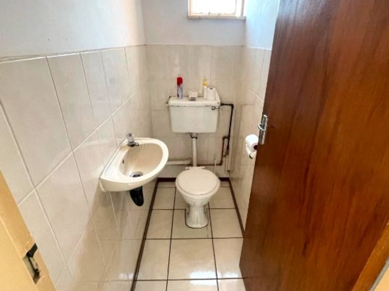 A compact, functional guest bathroom featuring a wall-mounted basin, ceramic tiling, and a standard toilet, requiring minor cosmetic updates.