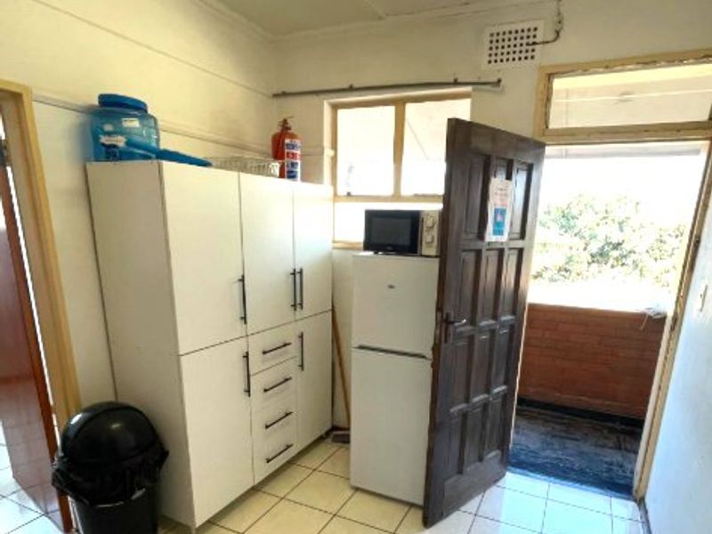 A functional scullery or utility area featuring tiled flooring, fluorescent lighting, and direct access to an outdoor balcony space.