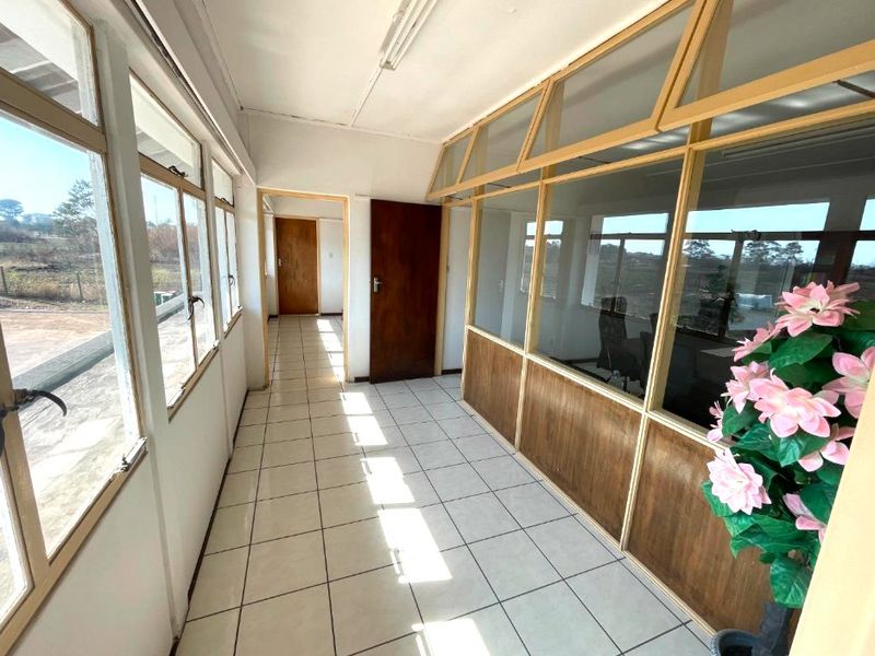 A bright, tiled commercial hallway featuring timber-framed glass partitions and access to adjacent office spaces.