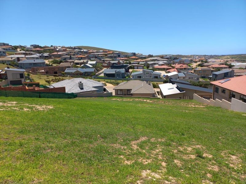 A wide-angle view overlooking a residential neighborhood from a sloped, grassy vacant plot.