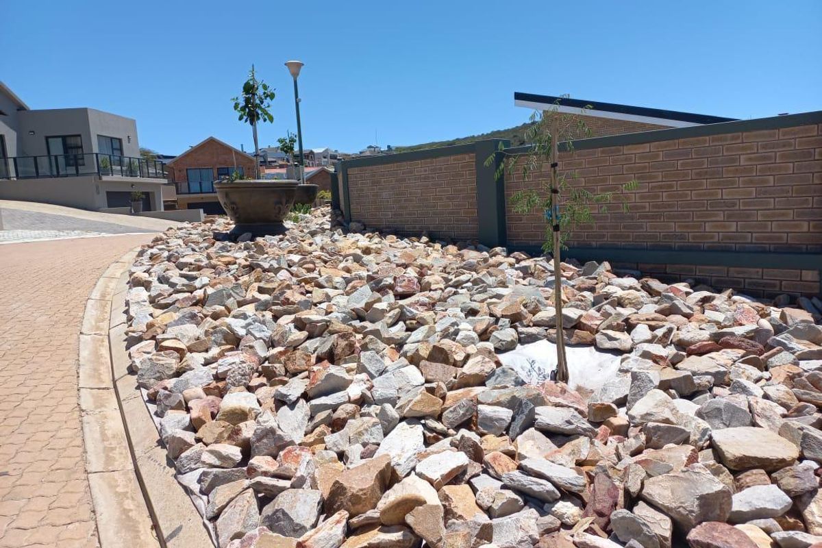 A well-maintained residential garden area featuring decorative rock landscaping, a brick boundary wall, and paved driveway access.