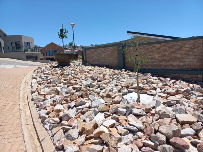 A well-maintained residential garden area featuring decorative rock landscaping, a brick boundary wall, and paved driveway access.