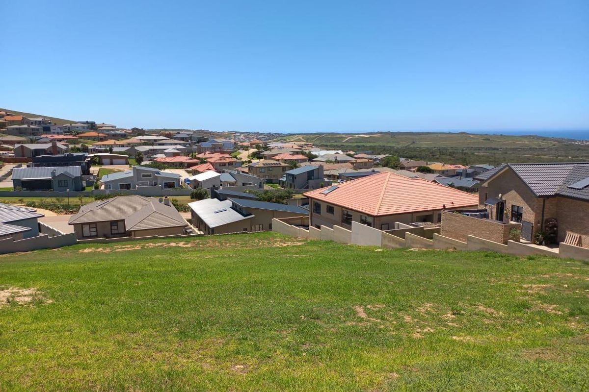 An elevated view overlooking a residential neighborhood with a sloped grassy foreground and distant coastal landscape.