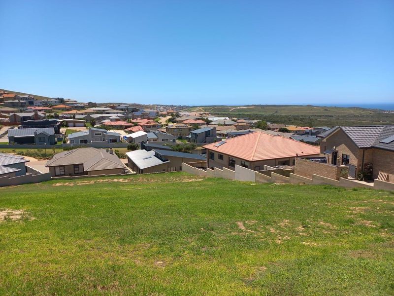 An elevated view overlooking a residential neighborhood with a sloped grassy foreground and distant coastal landscape.