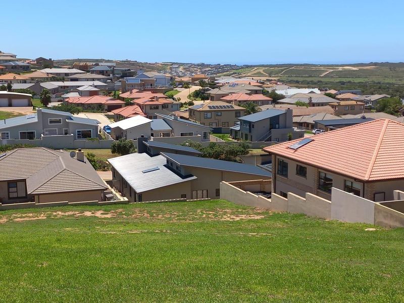 Elevated view overlooking a residential neighborhood with a sloped grass foreground and surrounding suburban housing.