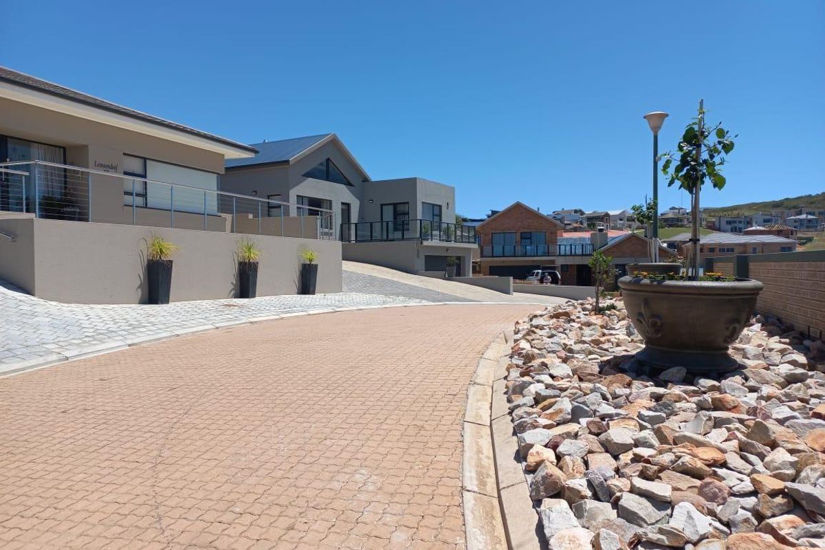 A view of a paved residential driveway and landscaped stone garden area leading towards modern homes in a well-maintained estate.