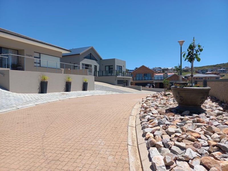 A view of a paved residential driveway and landscaped stone garden area leading towards modern homes in a well-maintained estate.