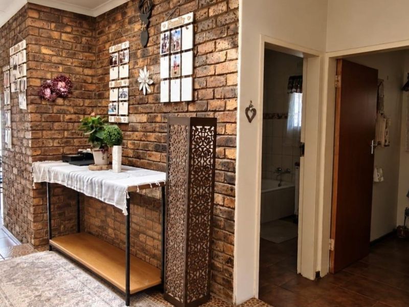 A hallway featuring a prominent exposed brick feature wall, tiled flooring, and access to adjacent rooms through doorways and an archway.