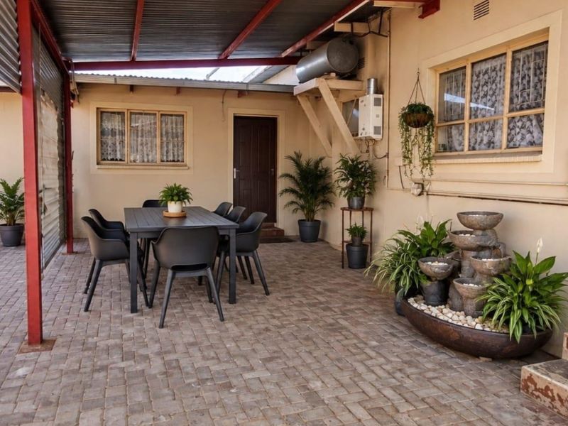 A covered outdoor patio area featuring paved flooring, a gas geyser, and direct access to the home, providing a functional space for outdoor dining.