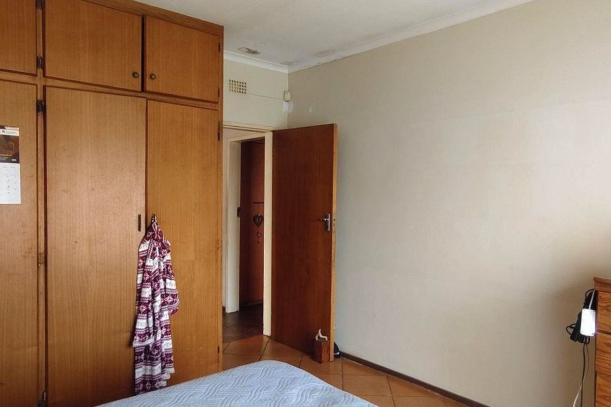 A bedroom featuring built-in wooden cupboards, tiled flooring, and visible ceiling water staining, offering potential for cosmetic updates.