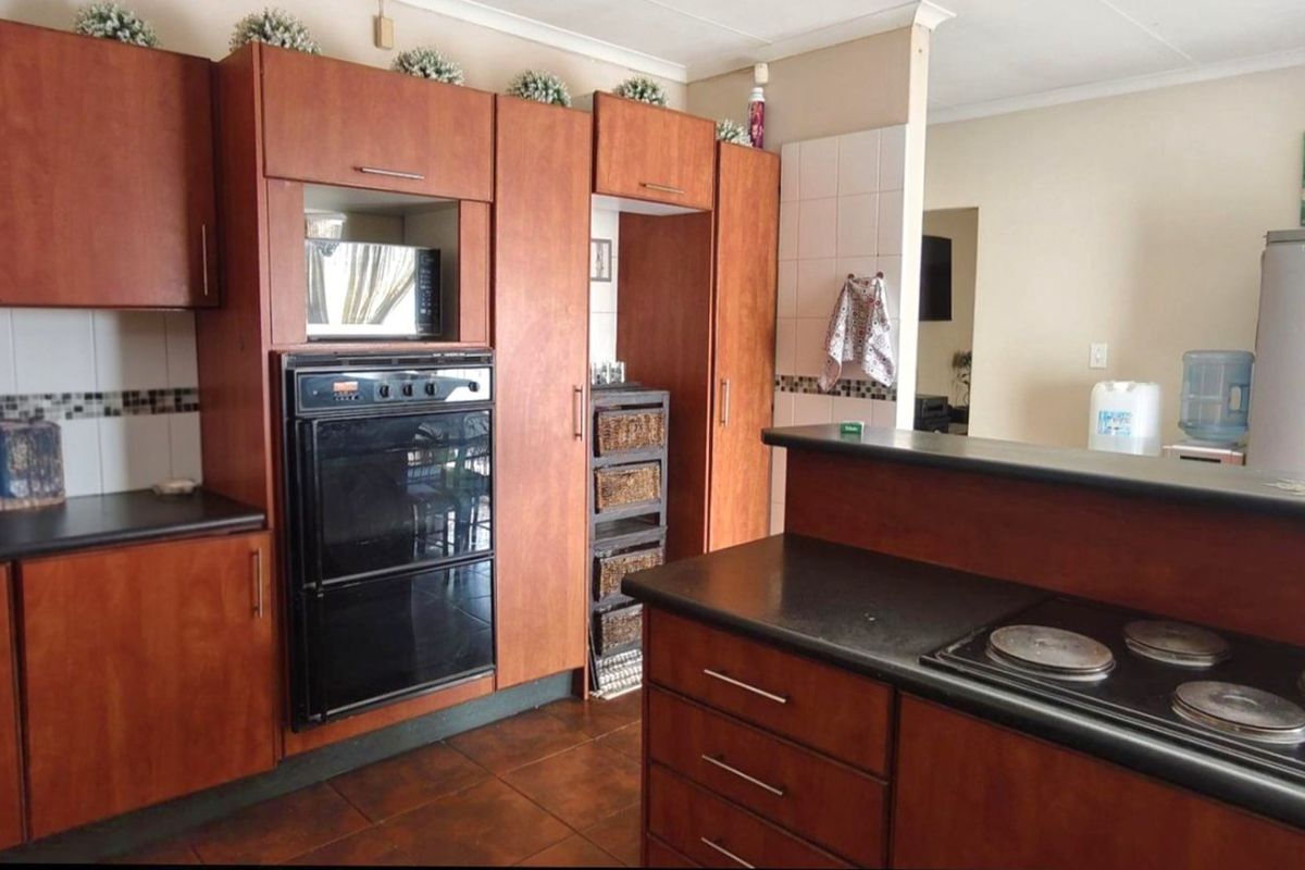 A functional kitchen featuring wood-look laminate cabinetry, built-in oven, electric hob, tiled backsplash, and dark countertops with tiled flooring.