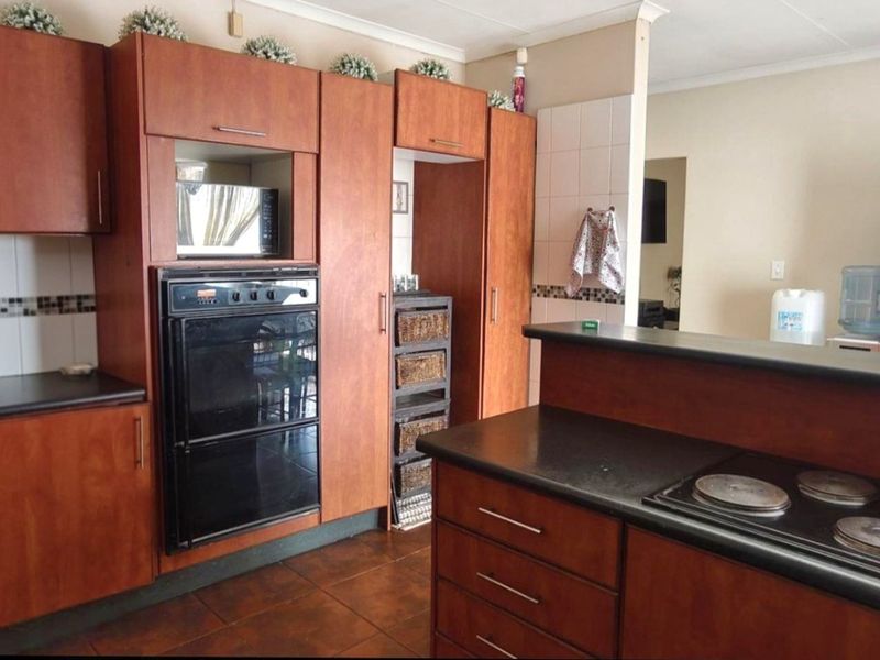 A functional kitchen featuring wood-look laminate cabinetry, built-in oven, electric hob, tiled backsplash, and dark countertops with tiled flooring.