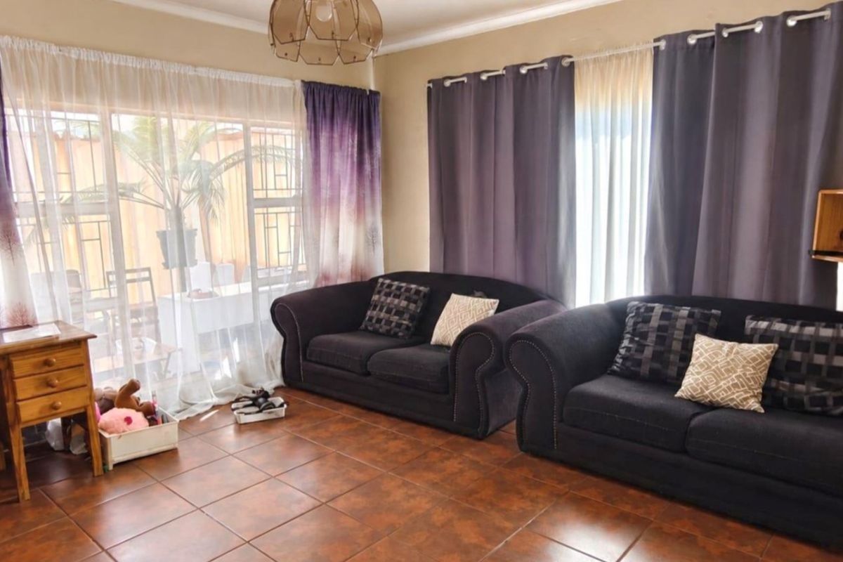 A living room featuring tiled flooring and a large sliding glass door with security gate, providing access to the outdoor area.