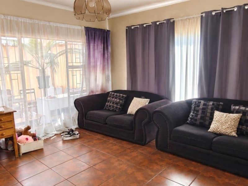 A living room featuring tiled flooring and a large sliding glass door with security gate, providing access to the outdoor area.