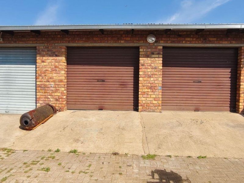 A triple garage featuring face brick construction, roller shutter doors, and an adjacent rainwater tank, set on a concrete driveway.