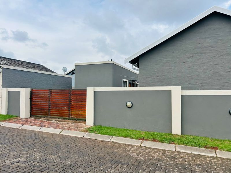 Front exterior view of the property featuring a modern grey boundary wall, timber slat gate, and paved driveway access.